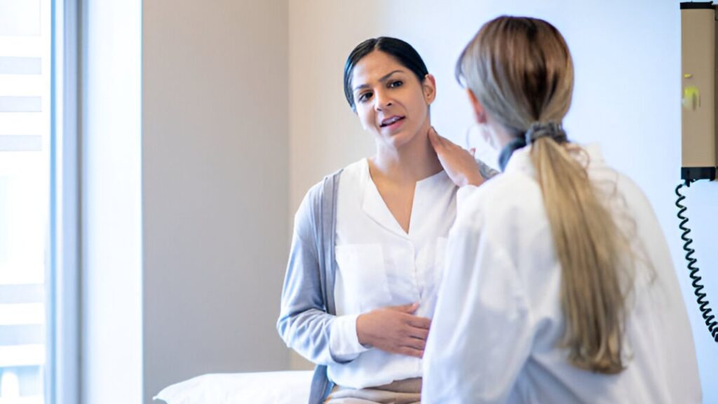 Chiropractor in San Antonio examines patient holding neck in clinical room with exam table.
