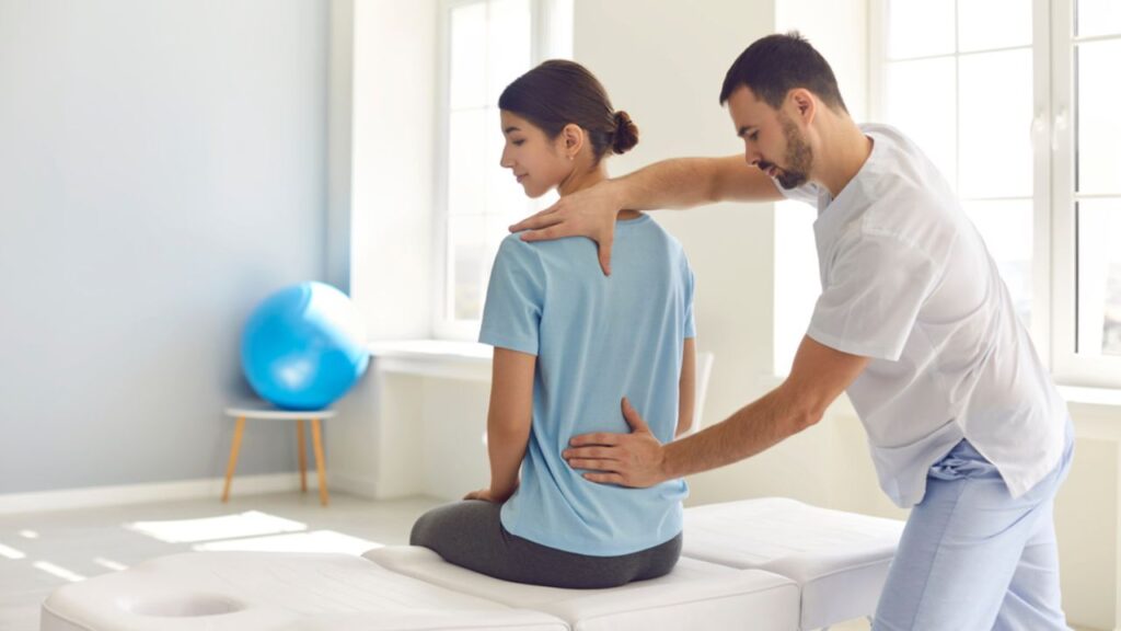 A therapist examining a seated patient's back, possibly a service offered by a Chiropractor In San Antonio.