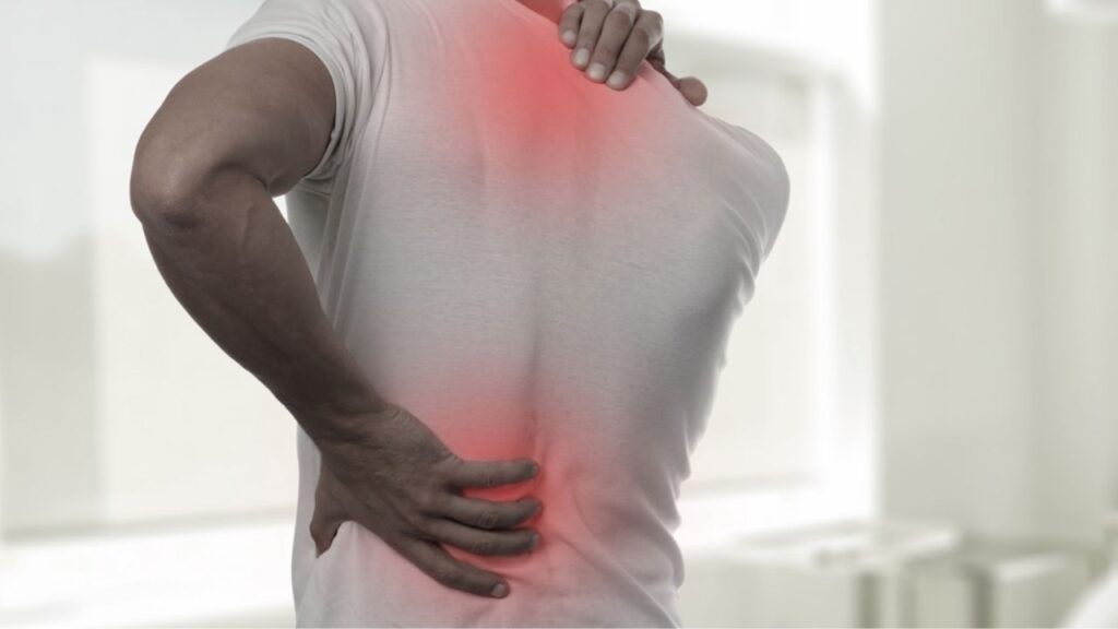 A person holds their lower back and shoulder, showing pain. Get effective Lower Back Pain Treatment Near Me at South Texas Spine & Joint Institute.