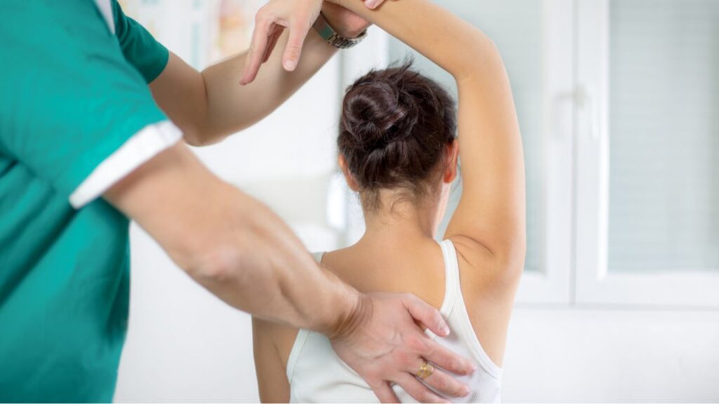 A therapist in green adjusts a woman's shoulder, providing effective Lower Back Pain Treatment Near Me at South Texas Spine & Joint Institute.